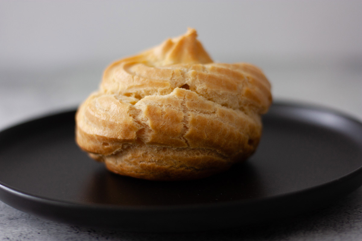 Oven baked zeppola on a black dish, ready to be filled with Italian crema pasticcera.