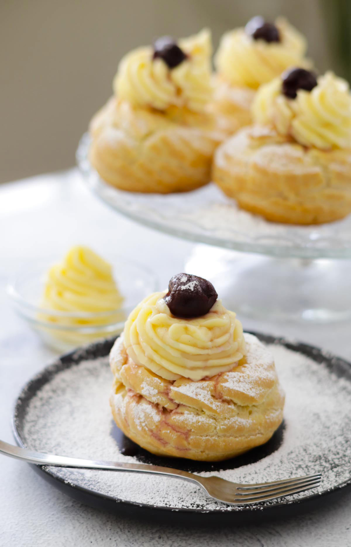 St Joseph's pastry in a close up, with pastry cream and amarena on top. In the background more zerppole.