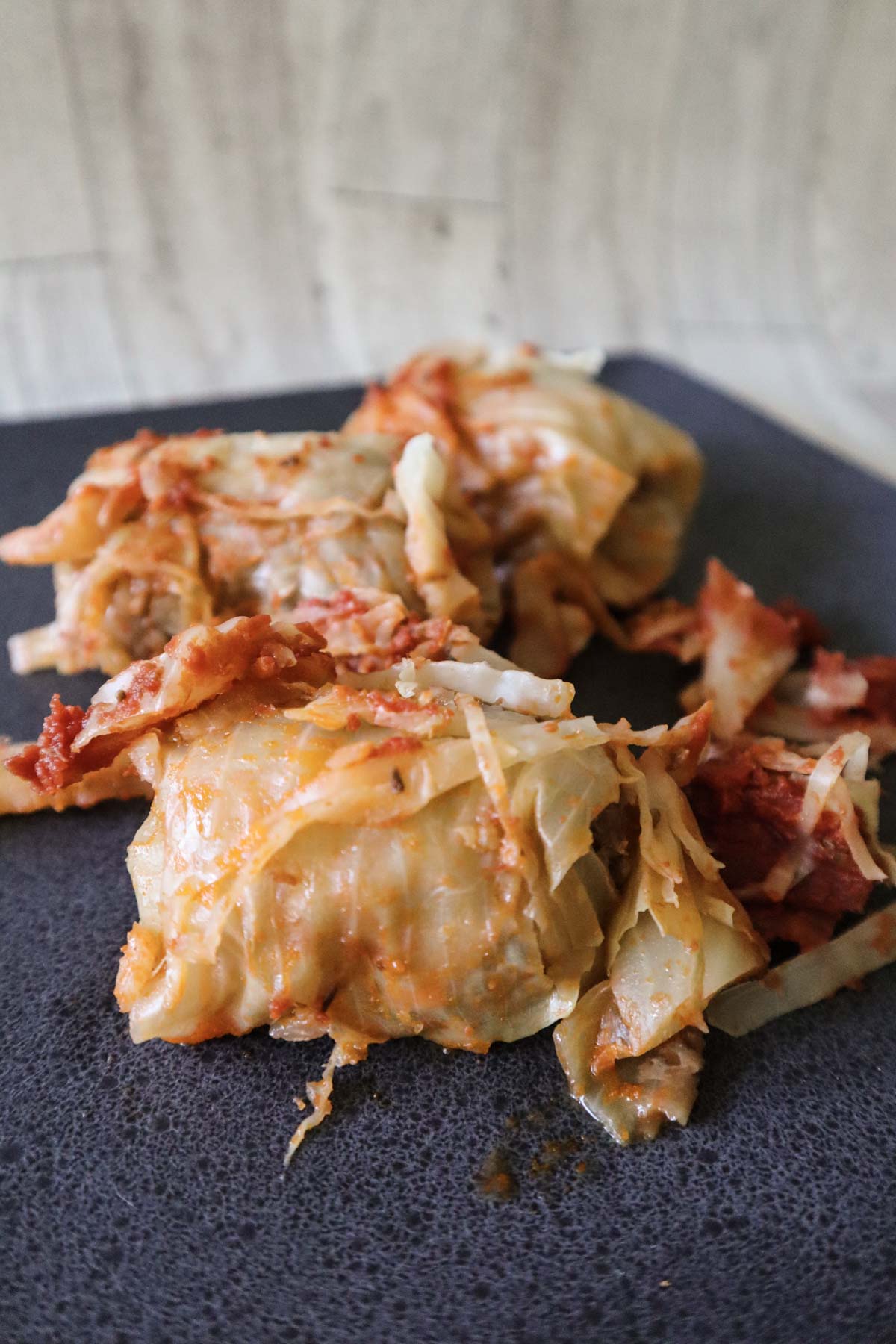 Italian cabbage rolls on a dark black plate served with extra cabbage on top and sauce.