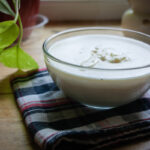 Béchamel sauce in a clear glass bowl on a kitchen towel.