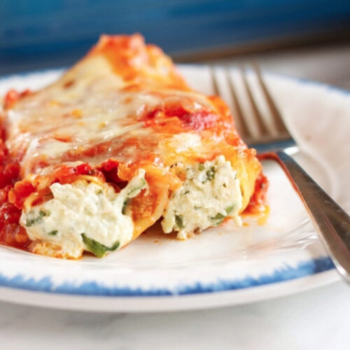 Cannerlloni ricotta and spinach on a white dish, with a fork on the side.
