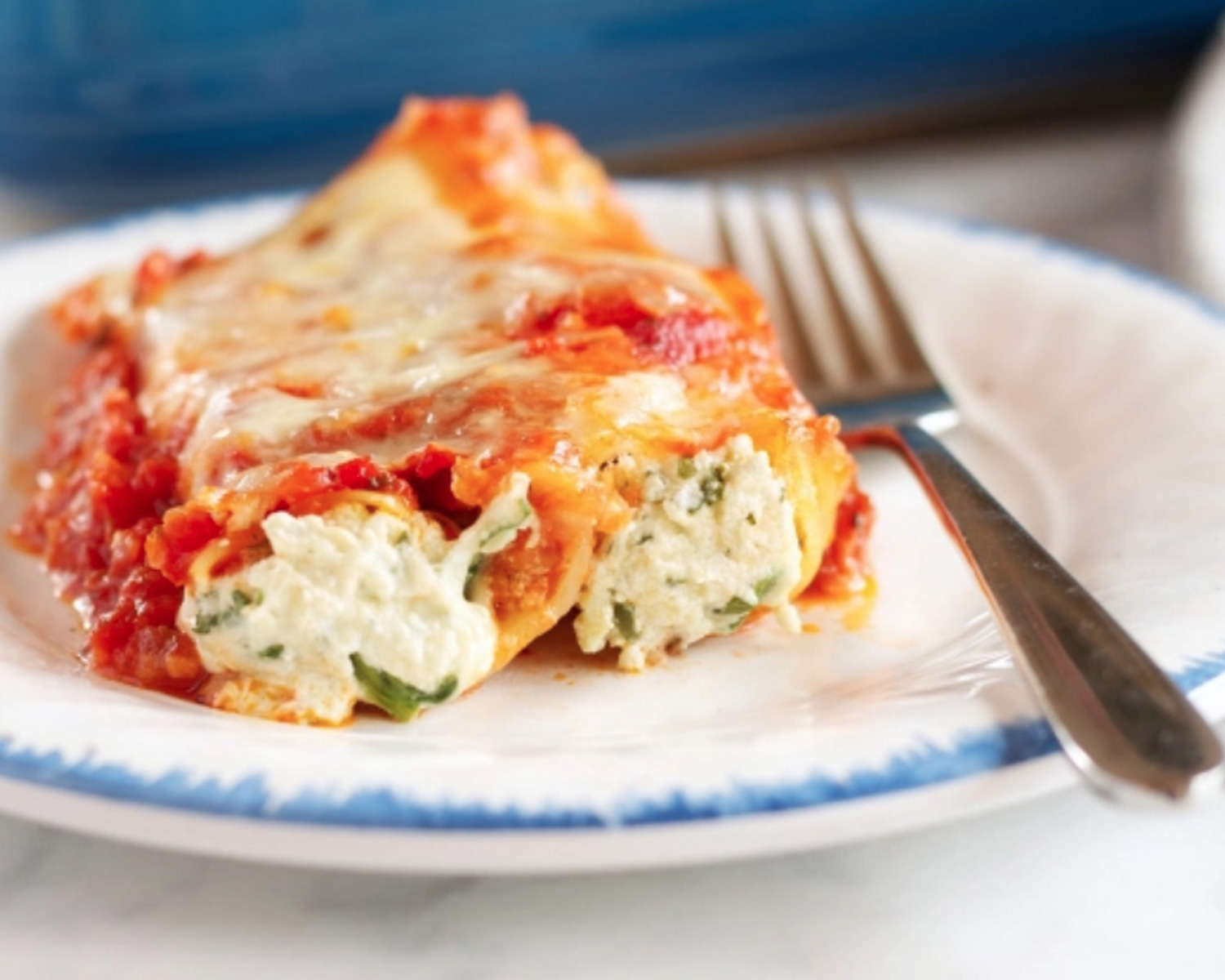 Cannerlloni ricotta and spinach on a white dish, with a fork on the side.