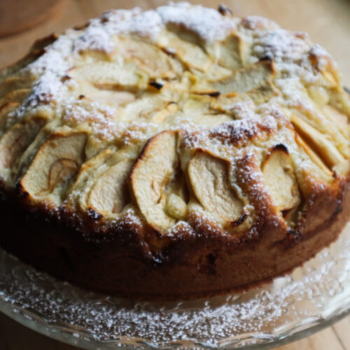 Italian apple cake on a glass dish dusted with powdered sugar, close‑up view