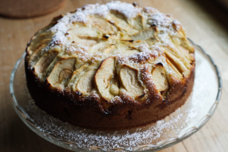 Italian apple cake on a glass dish dusted with powdered sugar, close‑up view