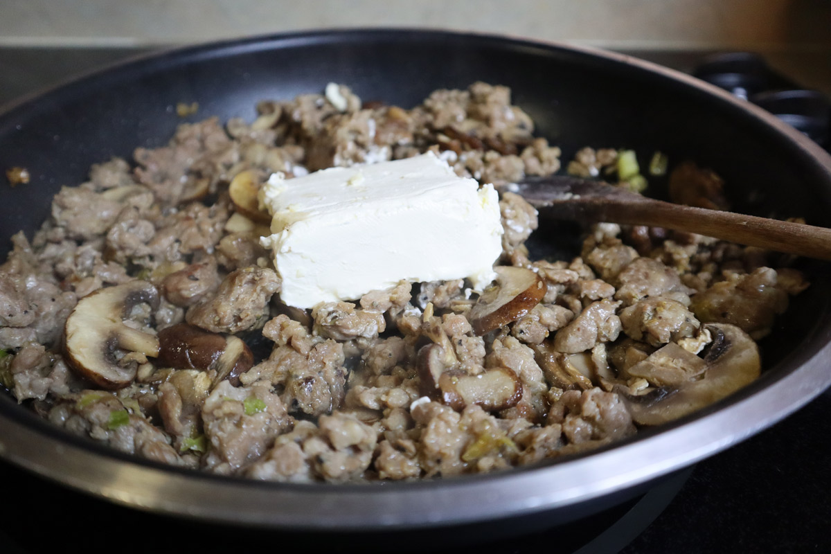 Cream Cheese with Italian Sausage and Mushrooms Cream cheese added to Italian sausage and mushrooms in a skillet before covering with the skilled lid.