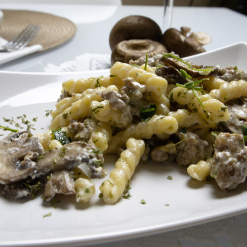 Creamy Italian sausage pasta with mushrooms and Parmesan served on a white plate.