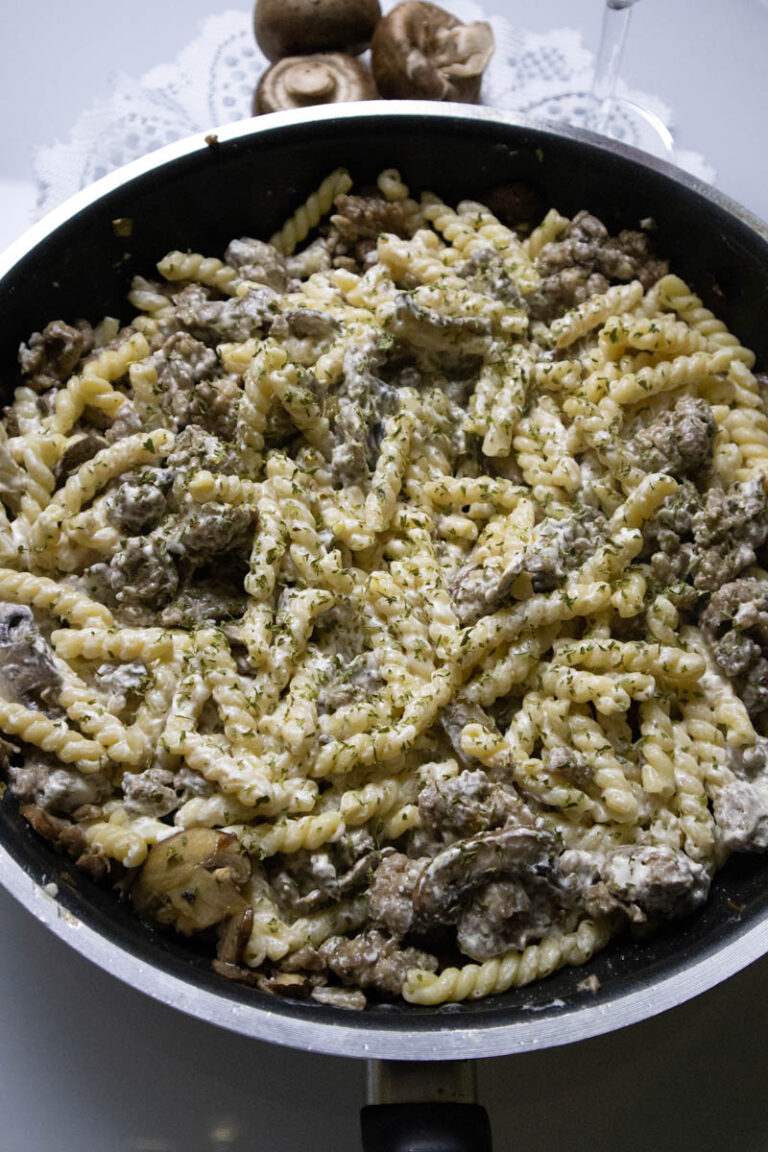 Creamy Italian sausage pasta with mushrooms cooking in a skillet and ready to be served.