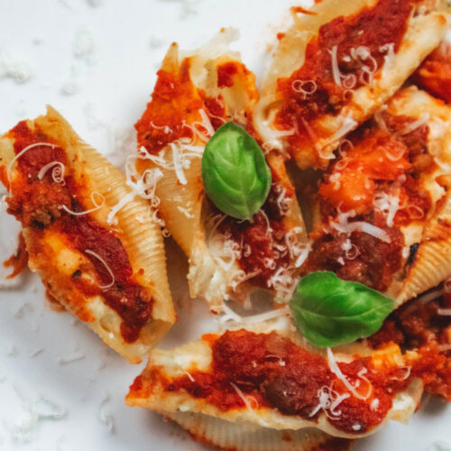 Close-up of baked Italian stuffed shells filled with ricotta and cooked ham, topped with meat ragù and melted cheese.