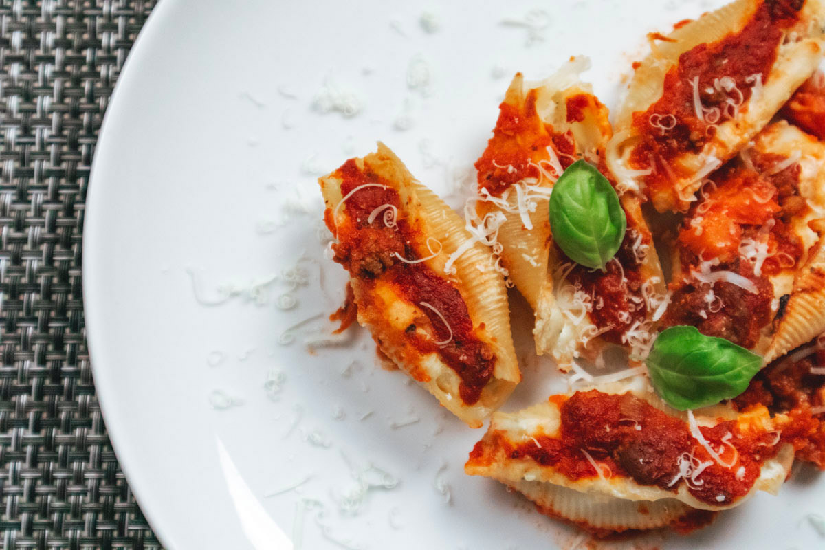 Close-up of baked Italian stuffed shells filled with ricotta and cooked ham, topped with meat ragù and melted cheese.